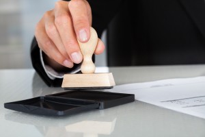 Close-up Of Business Man Hand Pressing Rubber Stamp On Document